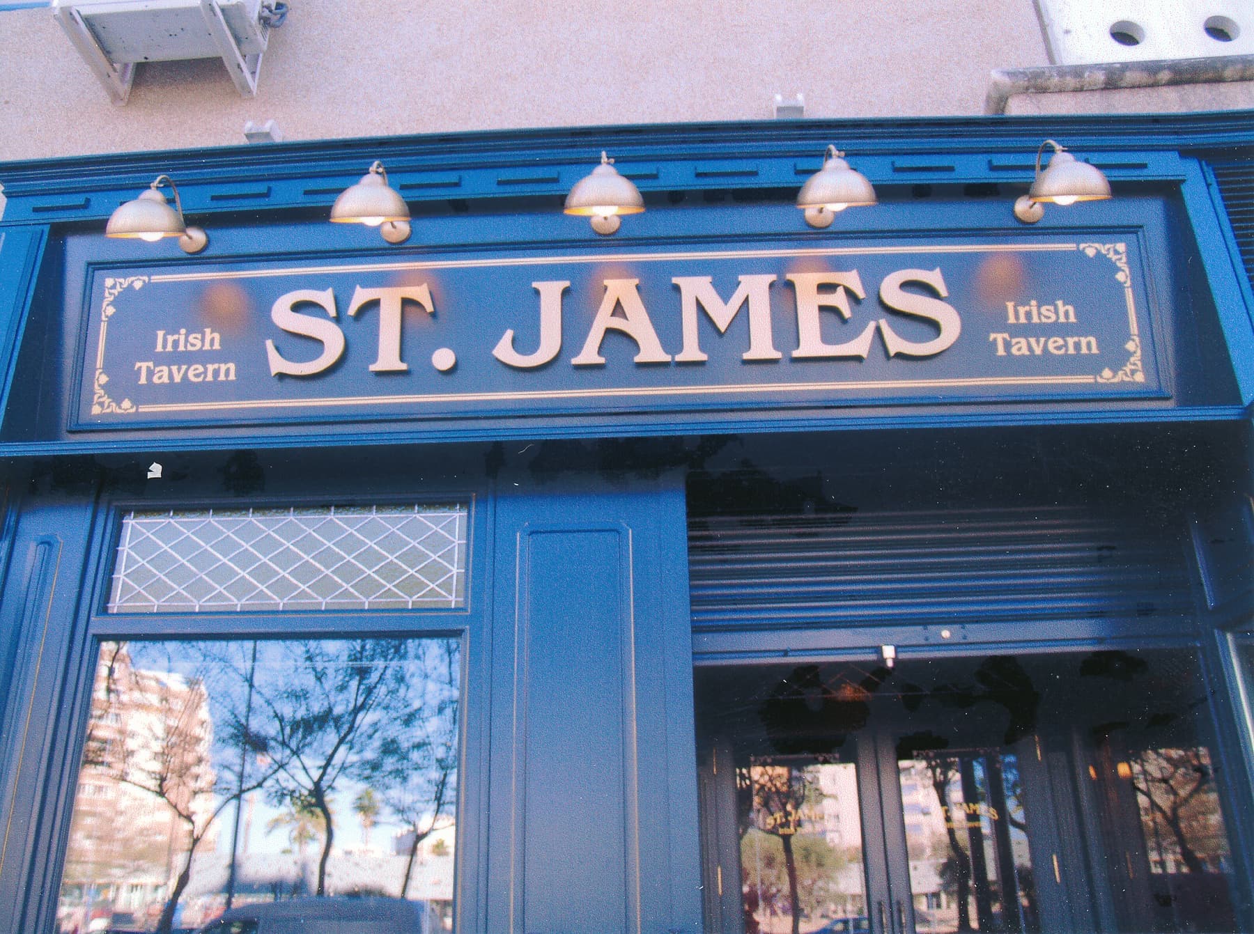 Fachada de la taberna irlandesa St. James con rótulo retroiluminado sobre madera azul