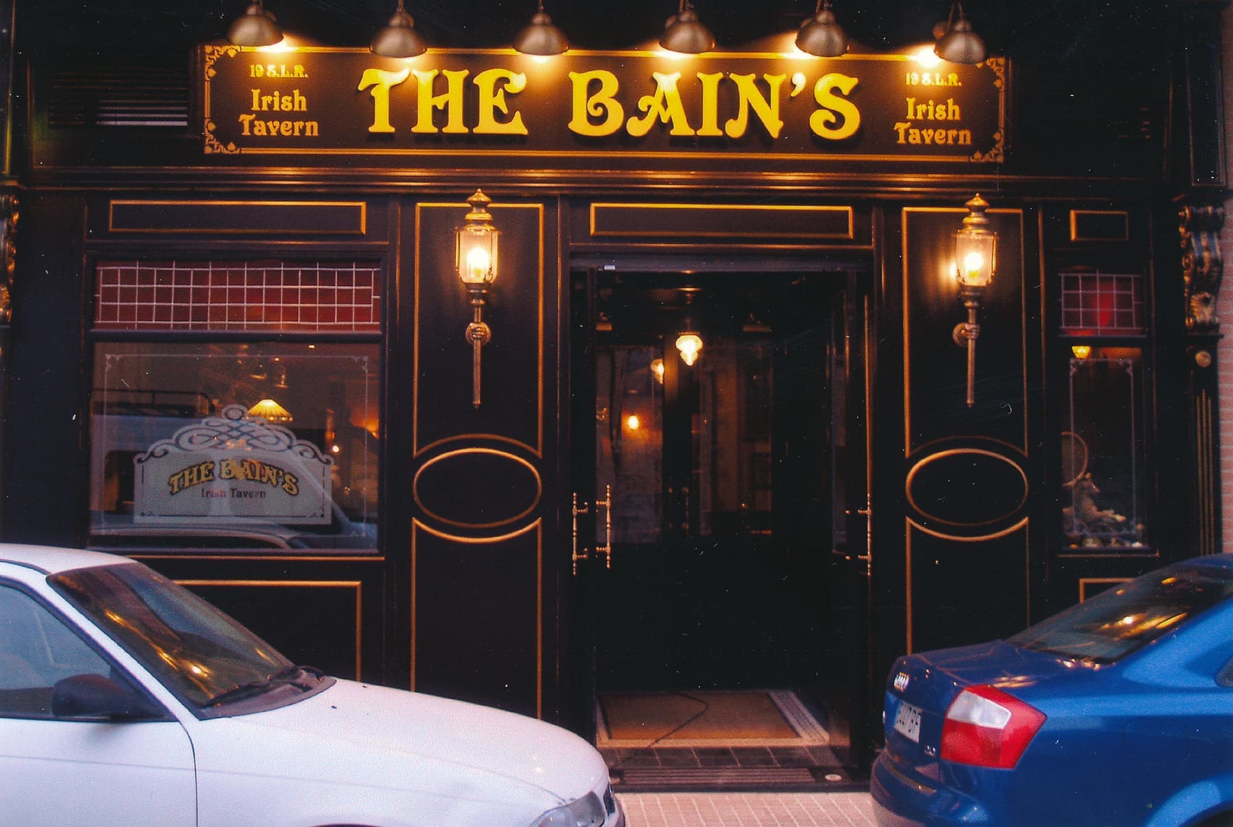 Fachada iluminada de The Bain's Irish Tavern con rotulación dorada sobre madera